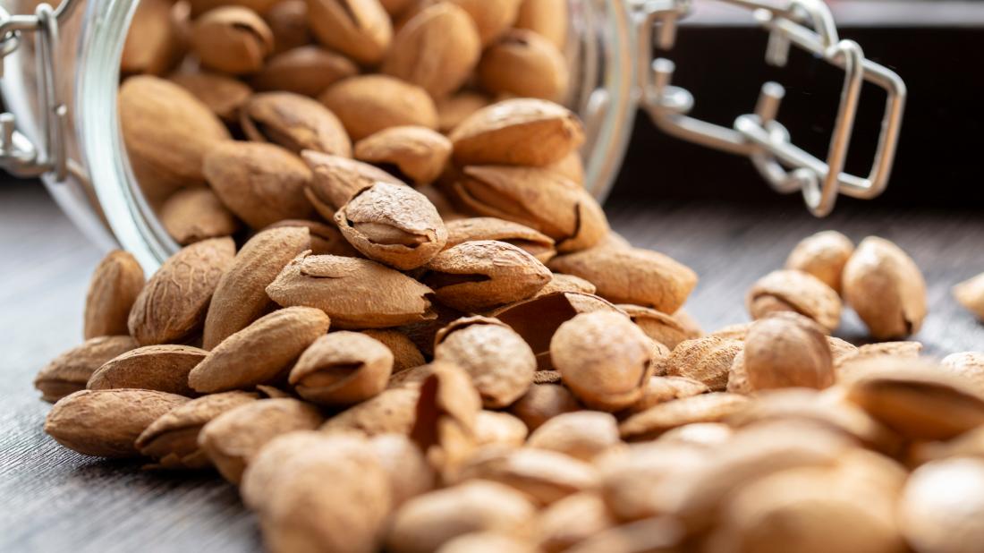 fresh raw almonds pouring out of glass jar onto a wooden table 1